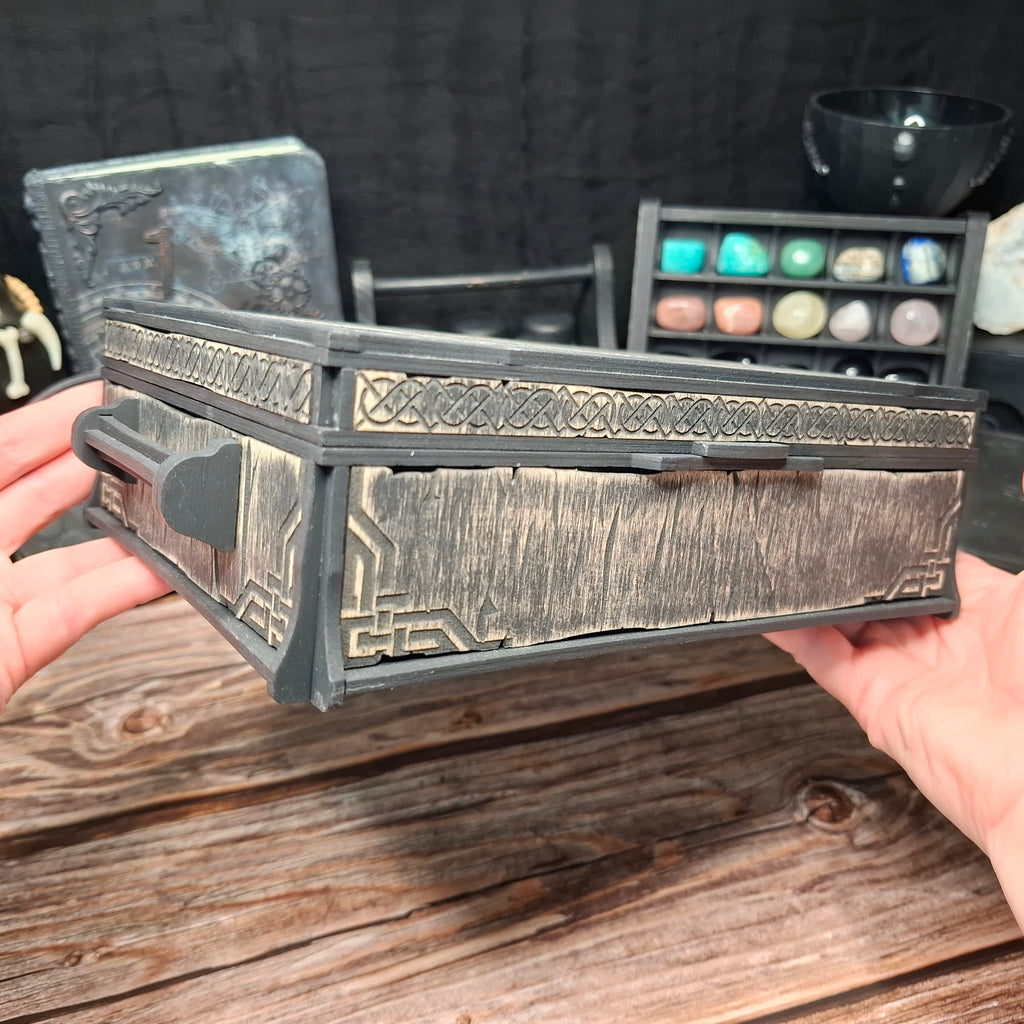 Corner view of a handcrafted Celtic ritual storage box held in both hands, showcasing the engraved Celtic details, wooden lid, and handcrafted finish.
